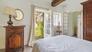 Une chambre à coucher avec un lit, une commode en bois, une lampe, un miroir et une fenêtre avec des rideaux.