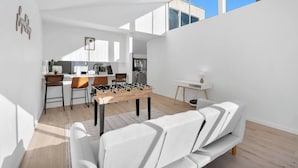 A modern living room with a foosball table, a sofa, and a kitchen in the background.