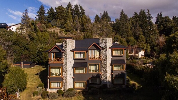 Hotel de vários andares com fachada em pedra e madeira, diversas varandas e paisagem montanhosa ao fundo.