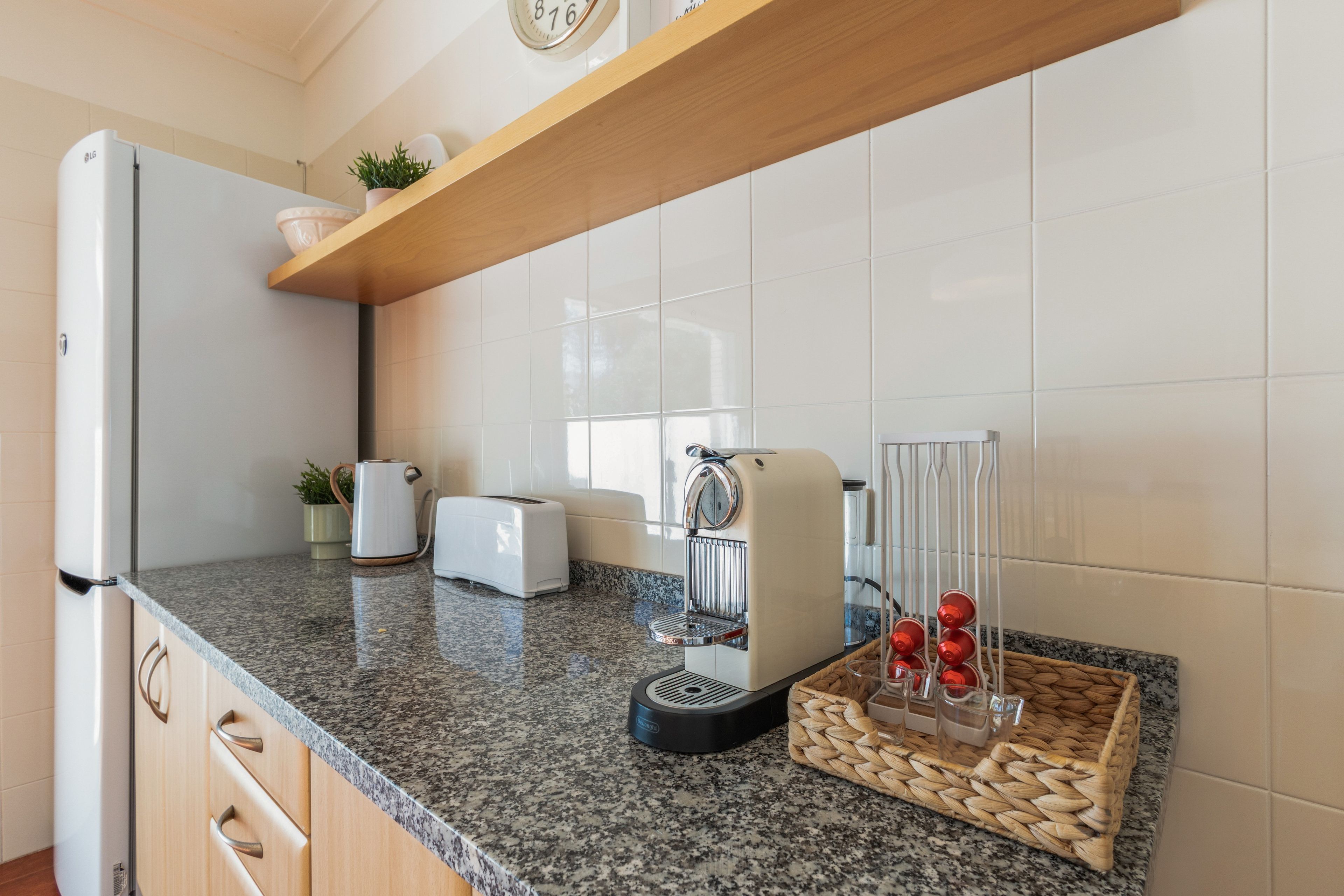 A modern kitchen with a granite countertop, a built-in refrigerator, a coffee maker, a toaster, and a basket with red bottles.