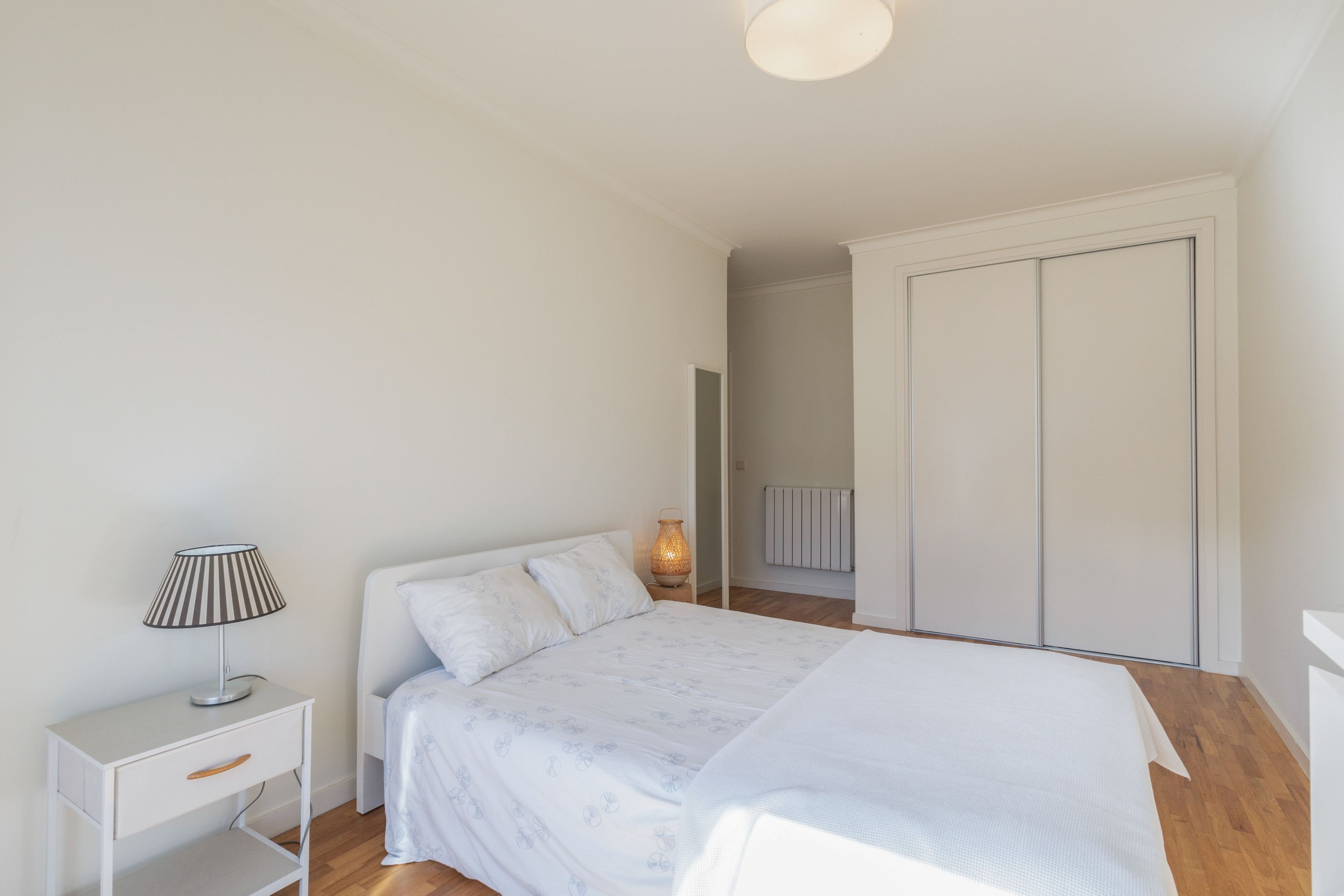 Un dormitorio con cama, mesita de noche, lámpara y armario.