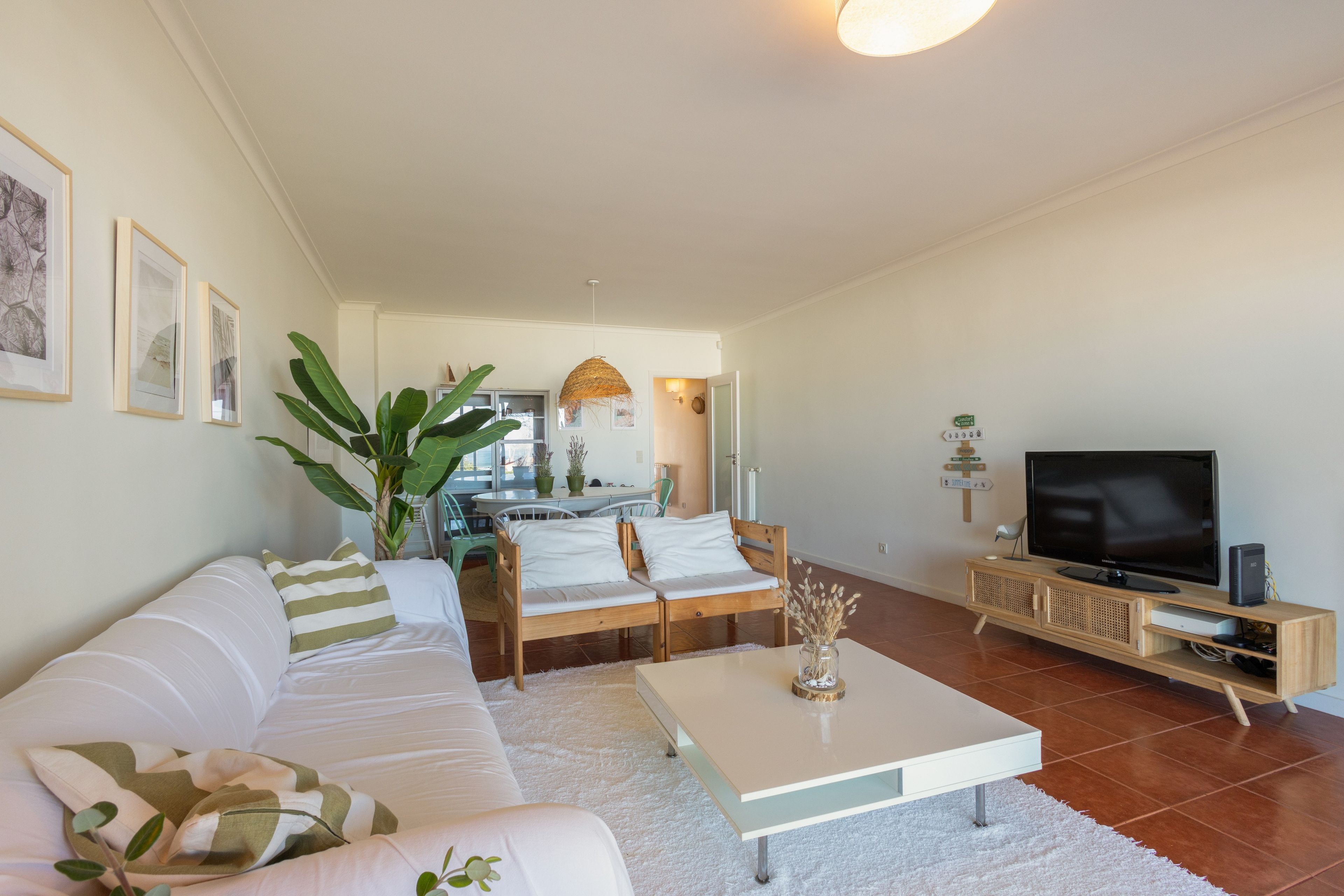 A modern living room with a sofa, coffee table, TV, and a dining area in the background.