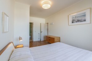 Een slaapkamer met een bed, nachtkastje, lamp, kaptafel en een ingelijste foto aan de muur.