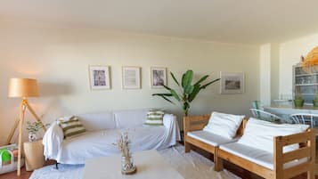 A living room with a sofa, a coffee table, a lamp, and a plant. There are framed pictures on the wall.