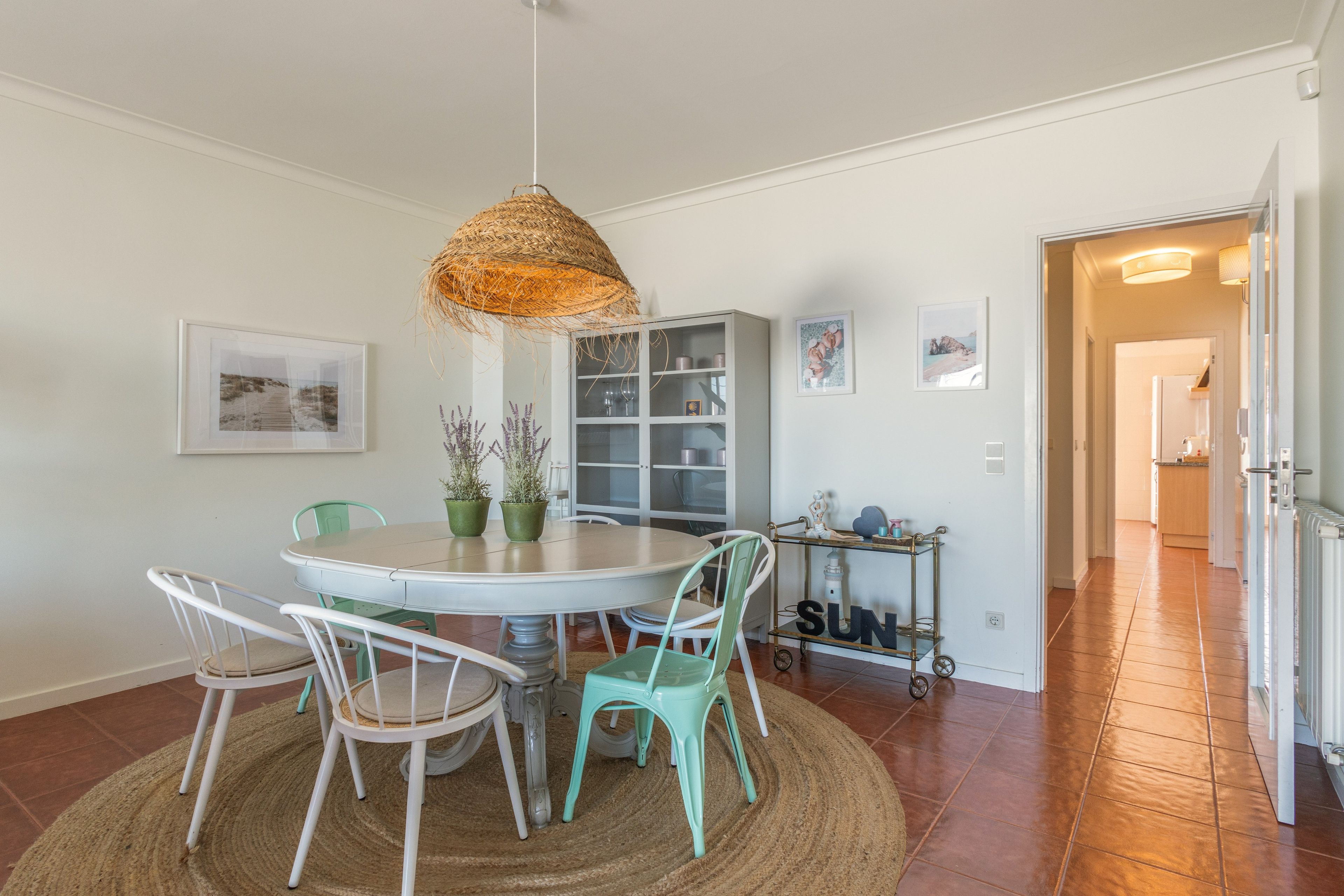 A dining area with a round table, chairs, a hanging light fixture, and a bookshelf.