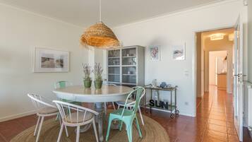 A dining area with a round table, chairs, a hanging light fixture, and a bookshelf.