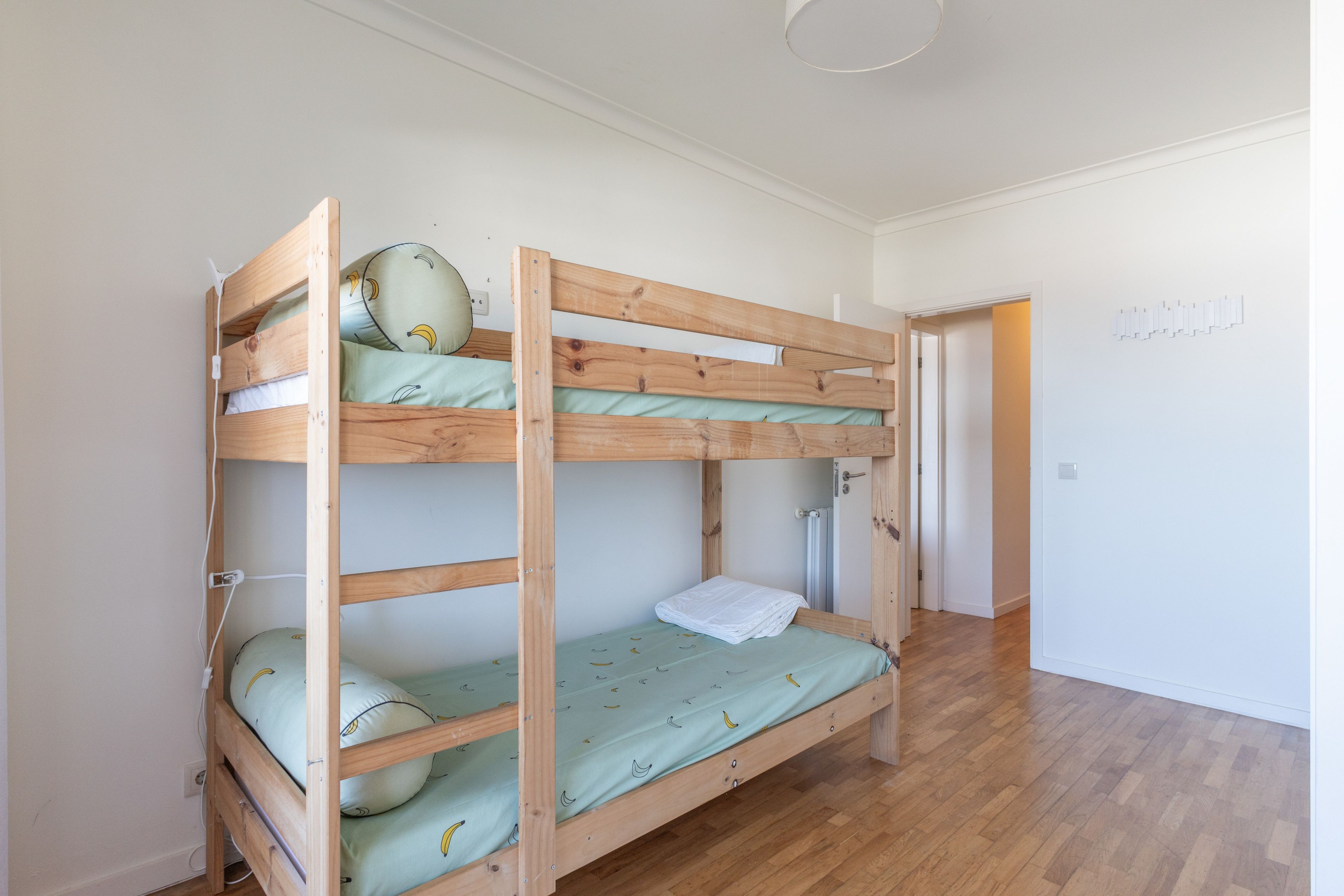 Een stapelbed met houten frame, een enkel matras en een kussen met bananenprint.