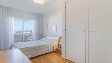 A bedroom with a bed, a desk, a chair, a wardrobe, and a view through a window.