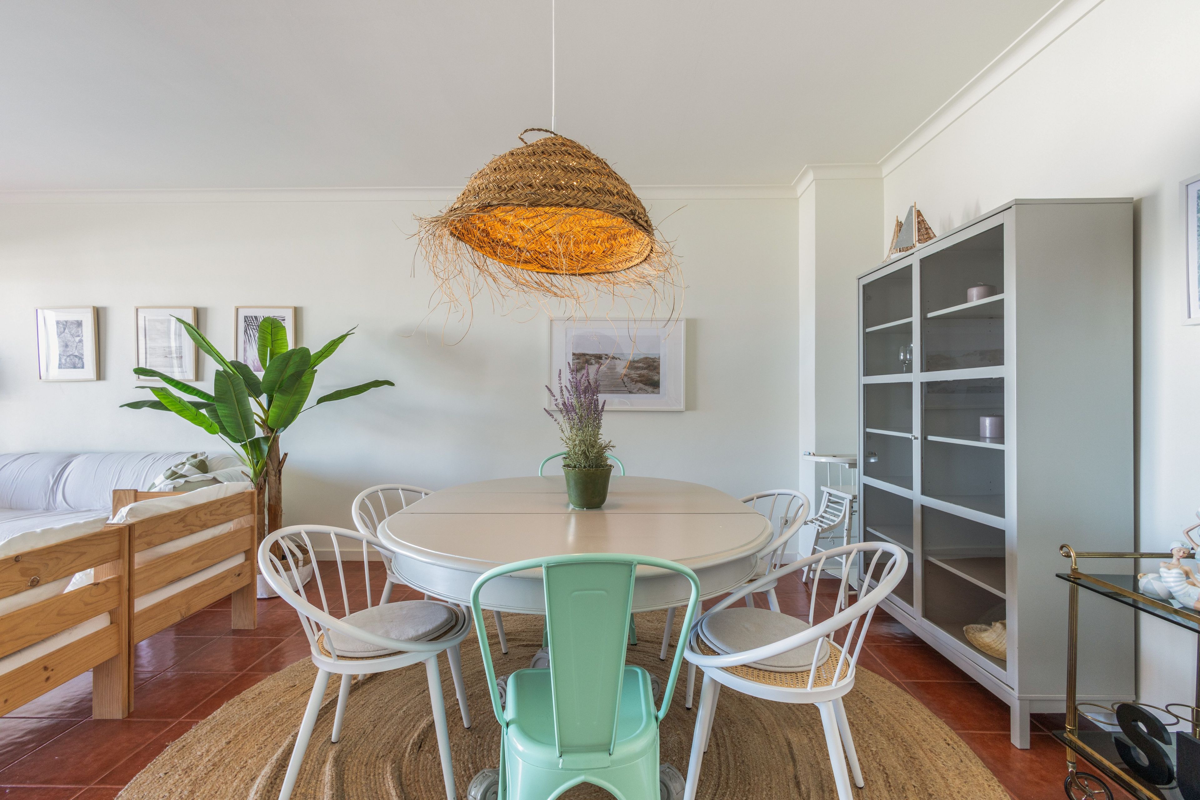 A dining area with a round table, white chairs, a hanging light fixture, and a cabinet with glass doors.