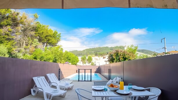 Un patio con piscina, sillas de descanso blancas y una mesa lista para comer.