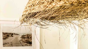 Una mesa de comedor con una cesta tejida colgando encima, un cuadro en la pared y un jarrón de vidrio con flores secas.