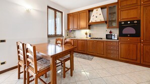 A kitchen with wooden cabinets, a dining table with chairs, a microwave, and a stove. - Apartment 'Lago' with Mountain View, Private Terrace and Wi-Fi (Dongo)