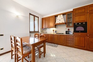 A kitchen with wooden cabinets, a dining table with chairs, a microwave, and a stove. - Apartment 'Lago' with Mountain View, Private Terrace and Wi-Fi (Dongo)