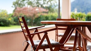 A wooden chair with a cushion, a table, and a view of greenery and mountains in the background. - Apartment 'Lago' with Mountain View, Private Terrace and Wi-Fi (Dongo)