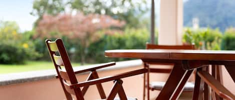 Une chaise en bois avec un coussin, une table et, en arrière-plan, une vue sur la verdure et les montagnes.