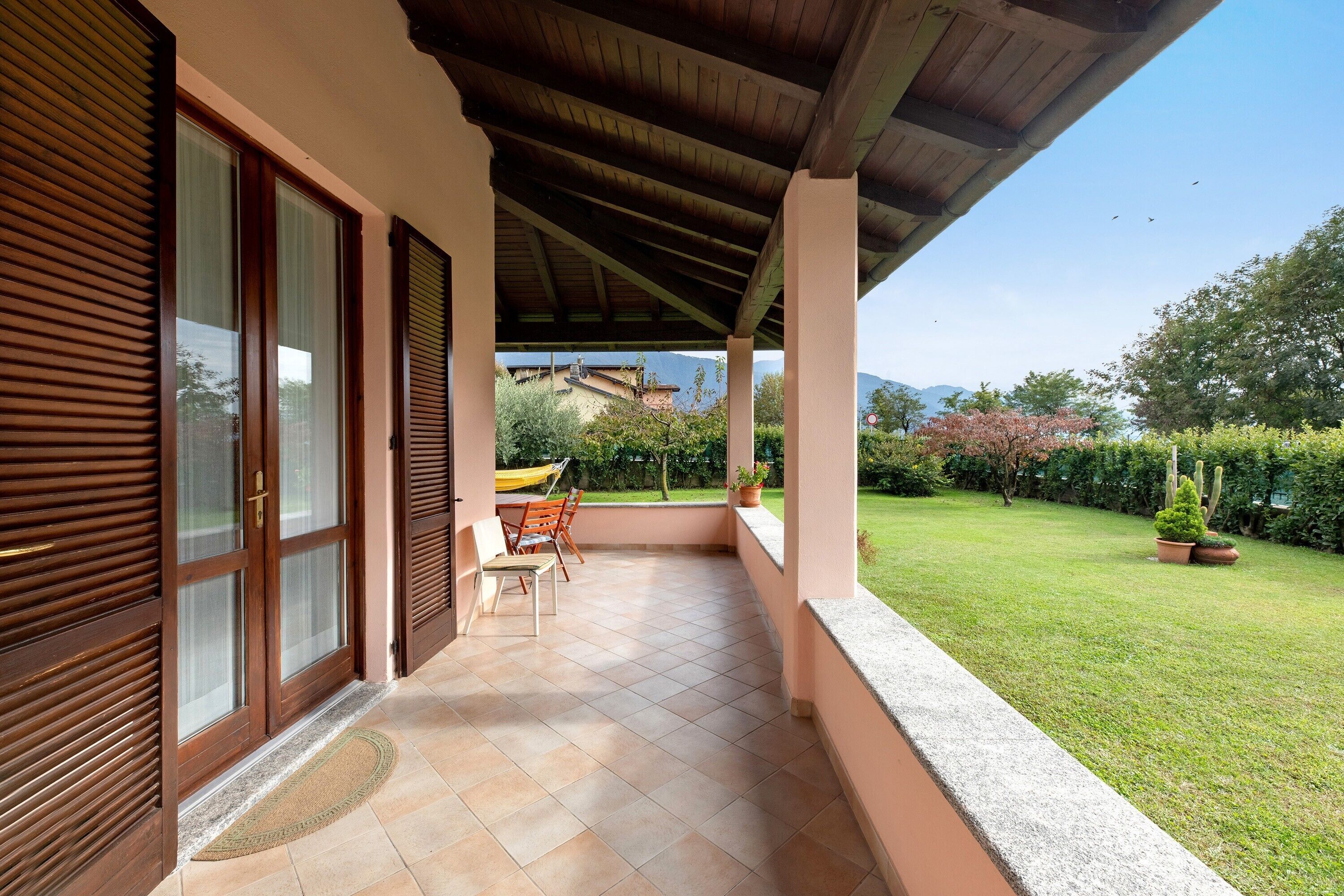 A covered patio with a view of a garden and mountains.