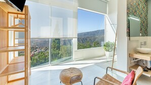 A modern room with a large window, a wooden chair, a wicker chair, and a bathroom with a large mirror and sink. - 'Villa bandama golf Agaete Suite-01' with sea views, Wi-Fi and air conditioning (santa brigida)