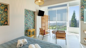 A bedroom with a bed, two chairs, a TV, a bookshelf, and a large window with a view. - 'Villa bandama golf Agaete Suite-01' with sea views, Wi-Fi and air conditioning (santa brigida)