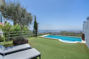 Una piscina con vista al mar, una zona ajardinada y una silla de descanso.