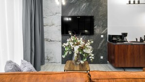 A modern kitchen with a marble backsplash, a flat-screen TV mounted above the counter, and a wooden dining table with a vase of flowers.