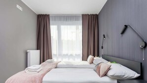 A modern hotel room with a bed, bedside table, and a wall-mounted lamp.