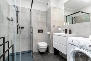 Ein modernes Badezimmer mit Duschkabine aus Glas, Toilette, Waschbecken und Waschmaschine.