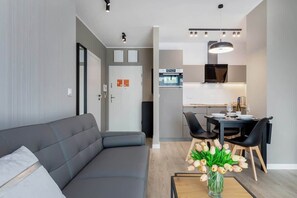 Un salon moderne avec un canapé gris, une table à manger avec des chaises et un coin cuisine équipé d’une cuisinière et d’un four.