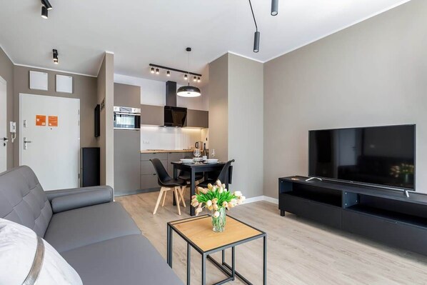 Un salon moderne avec un canapé, un téléviseur et un coin repas comprenant des chaises et une table.