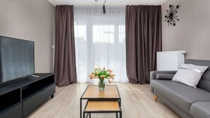 A modern living room with a flat-screen TV, a coffee table, a sofa, and a vase of flowers.