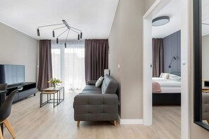 Una sala moderna con un sofá, un televisor y una mesita. Hay una cama en la habitación contigua.