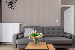 Un salon moderne avec un canapé gris, un vase de tulipes posé sur une table basse en bois et une horloge murale.