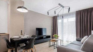 A modern living room with a sofa, a dining table with chairs, a TV, and a small side table with a vase of flowers.