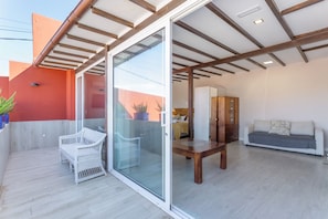 A modern living space with a sliding glass door, a wooden bench, a white sofa, and a wicker chair.