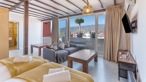 Quarto de hotel com cama, sofá, mesa, televisão e varanda com vista.