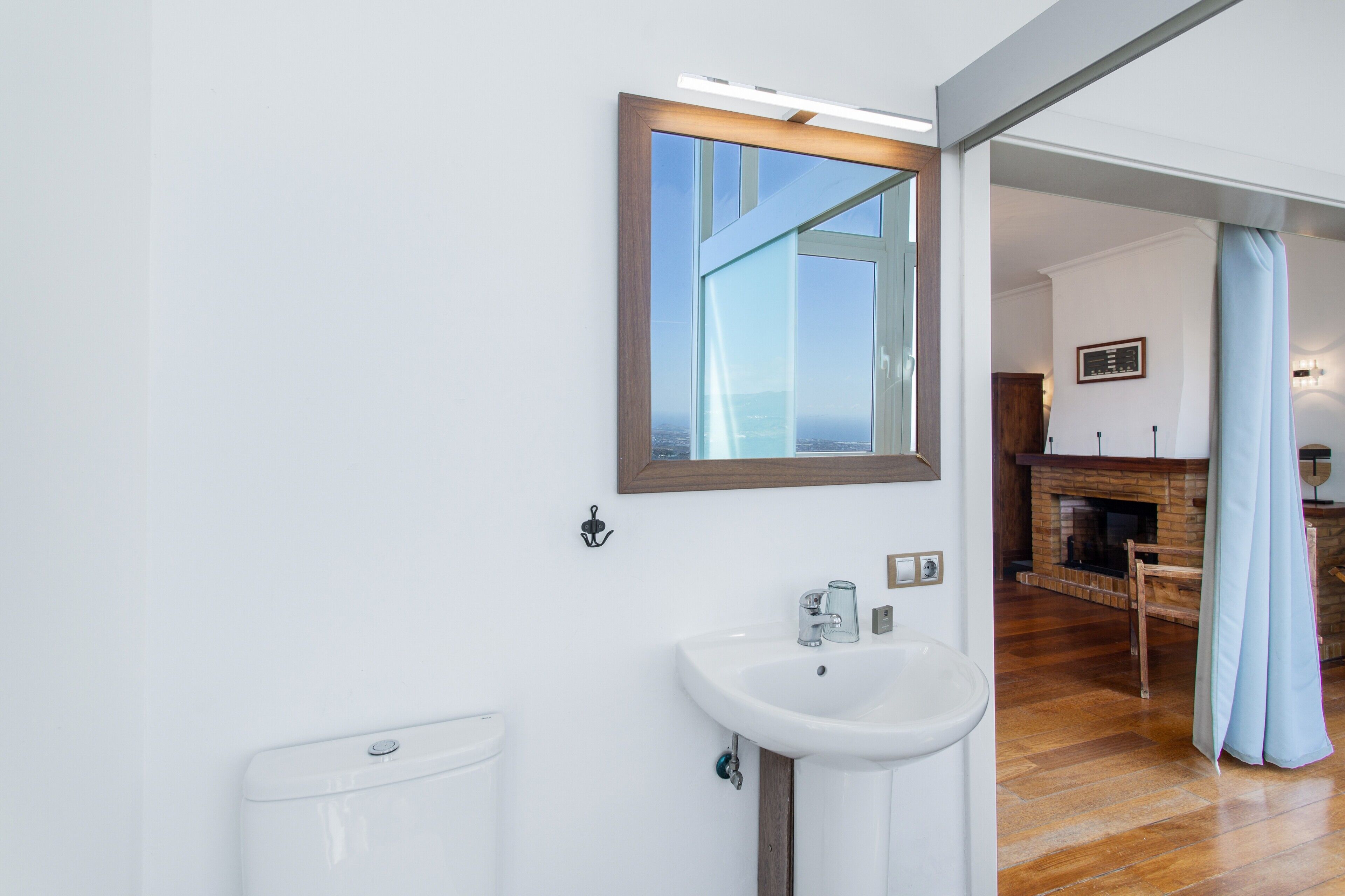 Un baño moderno con un lavamanos blanco, un espejo y vistas a una sala de estar con chimenea.
