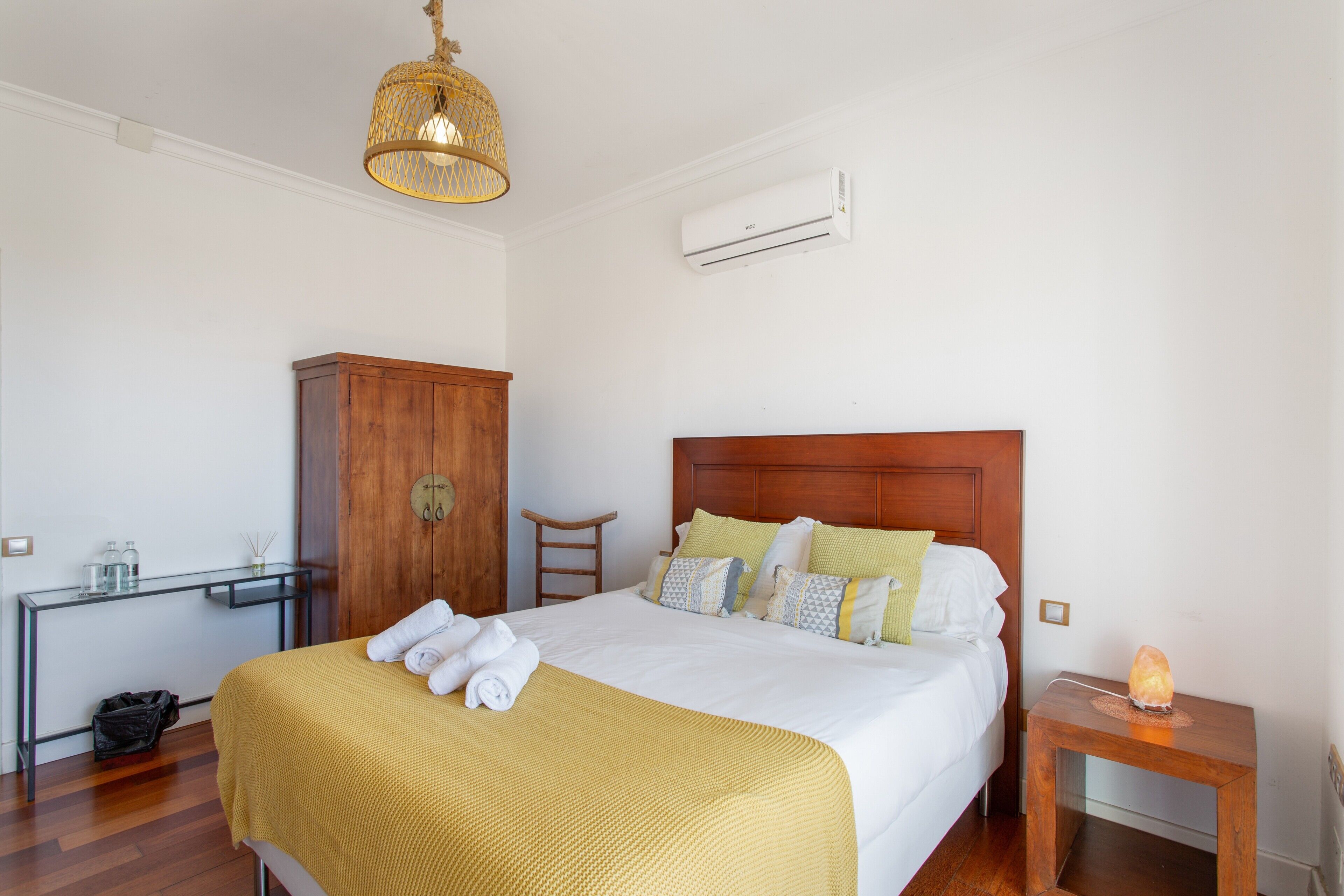 Een keurig opgemaakt hotelkamer met een bed, een houten hoofdbord, een nachtkastje, een bureau en een garderobe.
