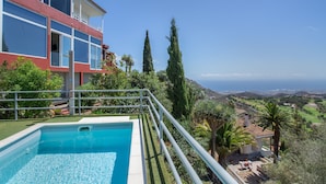 A pool with a view of the ocean, a two-story building with balconies, and a landscape with trees and hills. - 'Villa bandama golf Galdar-06' with sea views, Wi-Fi and air conditioning (santa brigida)