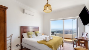 A hotel room with a bed, a balcony with a view, a TV, and a wooden chair. - 'Villa bandama golf Galdar-06' with sea views, Wi-Fi and air conditioning (santa brigida)