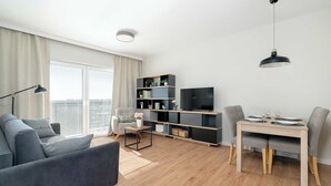 A modern living room with a grey sofa, a dining table with chairs, a TV, and a bookshelf. - Bright Apartment in Grunwald | Parking and Balcony (Poznań)