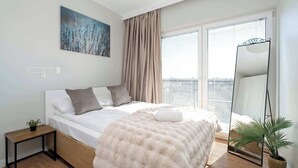 A bedroom with a bed, a nightstand, a mirror, and a window with blinds. - Bright Apartment in Grunwald | Parking and Balcony (Poznań)