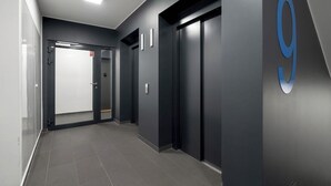 A hallway with two elevators, a door with a red sign, and a wall with a large number '9'. - Bright Apartment in Grunwald | Parking and Balcony (Poznań)