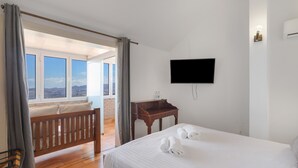 Habitació d'hotel amb llit, una banca de fusta, escriptori, televisió de pantalla plana i vistes per una finestra gran.