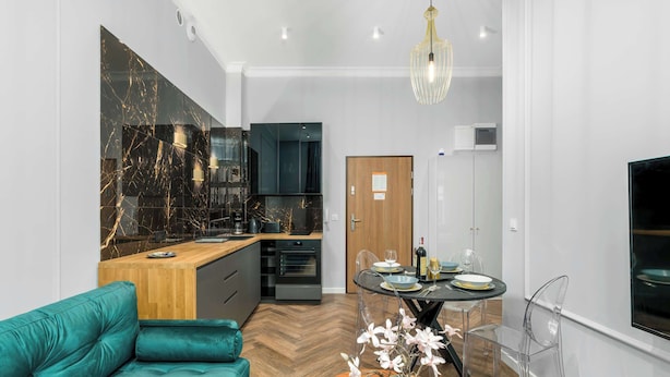 Una cocina moderna con salpicadero de mármol, una mesa de comedor de madera con sillas transparentes y un sofá color turquesa.