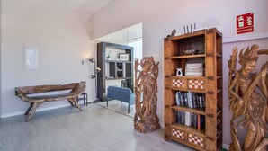 Een kamer met een houten bankje, een boekenplank vol boeken en een decoratief houten beeldhouwwerk.
