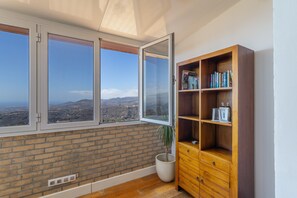 A room with a large window, a brick wall, a wooden bookshelf, and a potted plant.
