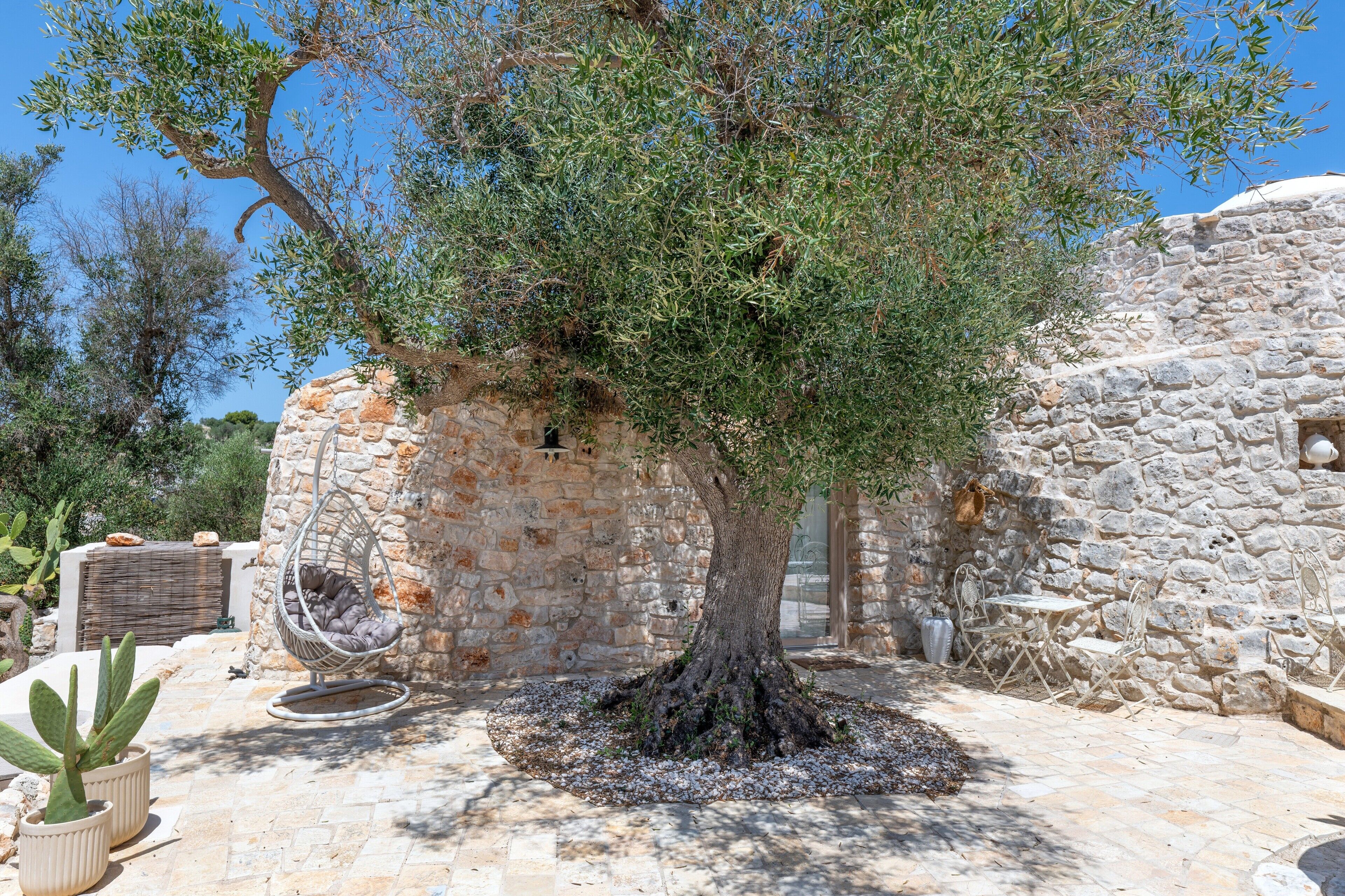 Ein Steinhaus mit einem Baum in der Mitte, einem Hängekorbstuhl und Gartenmöbeln.