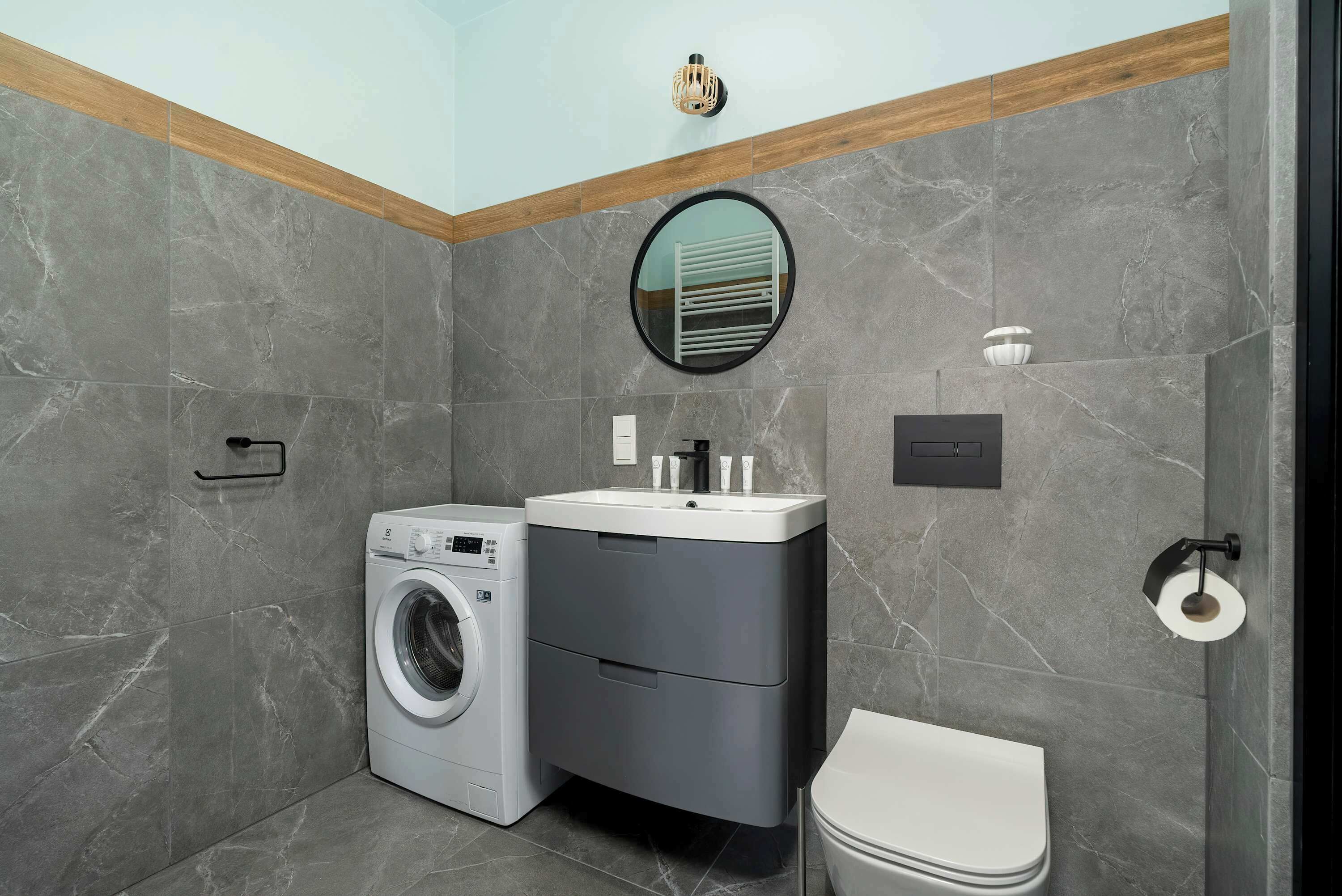 Une salle de bain compacte avec des murs en marbre gris, un lave-linge, un lavabo moderne et des toilettes.