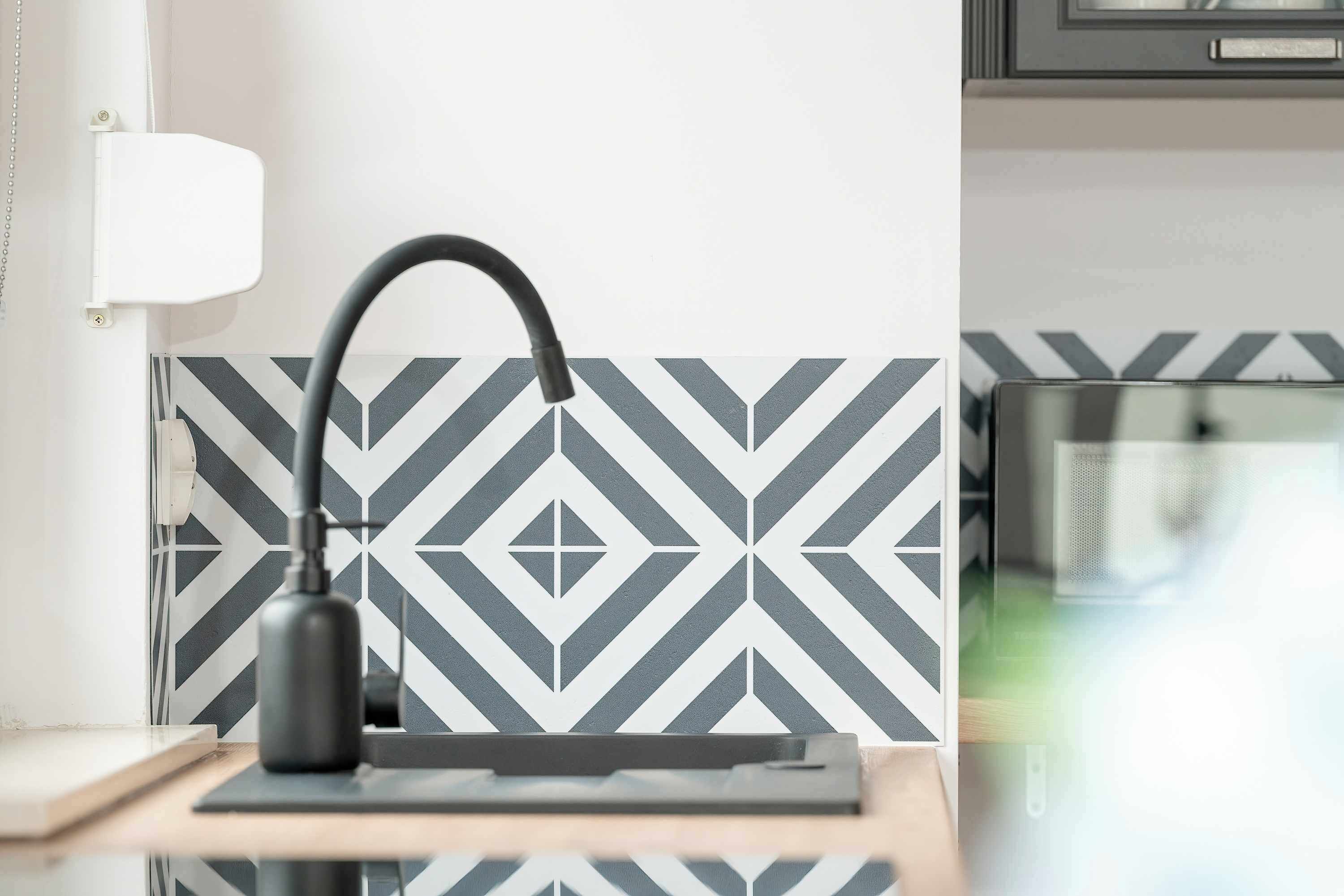 A modern kitchen with a black and white patterned backsplash, a black faucet, and a wooden countertop.