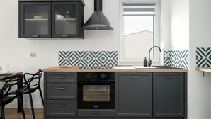 A modern kitchen with dark cabinetry, a built-in oven, and a window with blinds. - Stylish Apartment in Poznan | Terrace | Parking (Poznań)