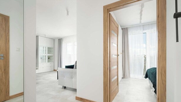 A modern hotel room with a large bed, a white wardrobe, and a glass door leading to a balcony. - Modern Apartment | Air Conditioning, Parking, Balcony (Poznań)
